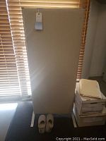 Large light beige fabric office divider, supported by metal legs, standing upright in front of window blinds.