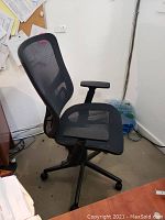 Side view of black mesh office chair showing ergonomic backrest, armrests, and caster wheels.