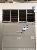 Front view of first metal filing box showing multiple horizontal shelves on top and two large drawers below.