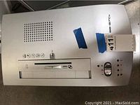 Top view of the shredder showing the control panel with dial, slot for shredding, and ventilation holes. Blue tape and a lot tag are attached on top.