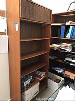 Two wooden bookshelves with multiple shelves, one with woven baskets on the upper shelf and some books and papers inside.