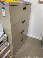 Side view of beige 4-drawer lateral file cabinet with black handles, showing the cabinet height and depth.