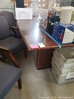 Side view of the wooden conference table showing scratches and solid wooden leg.