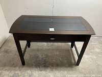 Front view of the whole office table showing the glass inset top and wood frame with drawer under.