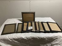 Set of ten wooden picture frames laid out on white sheet. Frames vary in wood finish and color, measures about 12x10 inches each.