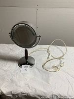 Electric makeup mirror with chrome finish, circular dual-sided mirror on stand, visible power cord with switch.