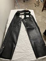 Full view of black leather motorcycle chaps laid out flat showing entire length and design details.