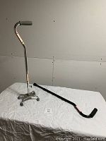 Photo showing two walking canes: one with quad base and metal parts, the other a single black cane.