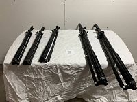 Six folded tripods of varying sizes laid on a table covered with white cloth