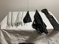 Wide shot of 11 reflector umbrellas (9 white, 2 black) and one black carrying bag placed on a white sheet.