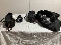 Overview of multiple camera lighting equipment and bags, including one bag with broken zipper, laid on white cloth against wall.