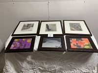 Six wood picture frames displayed on table, three larger and three smaller, with various black and white and color images under glass fronts.