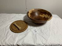 Photo of entire set showing a large segmented wooden bowl, circular wooden cutting board, and wooden pestle on a white cloth.