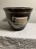 Large brown planter pot wrapped in plastic, showing overall shape and size.