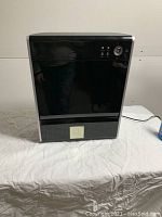 Front view of the air purifier showing black glossy panel and silver edges on a white table.