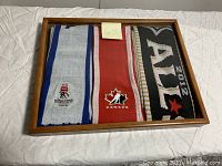 Framed display of three scarves side-by-side under glass showing event logos and colors.
