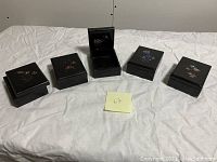 Full set of five small black lacquered wood boxes with floral mother of pearl inlay designs shown on a white cloth background.