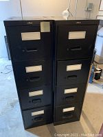 Front view of two black metal filing cabinets showing four drawers each with label holders and handles.