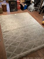 Full view of the rug laid flat on wood floor in room, showing overall size and geometric design pattern with diamond lattice.