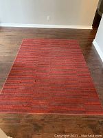 Red textured rectangular rug on a wood floor to show entire rug and condition.