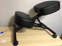 Side angle view of the black ergonomic kneeling chair showing the adjustable frame, padded seat, and knee cushions with caster wheels.