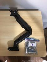 Monitor mount arm laid flat on wood desk with hardware bag included.