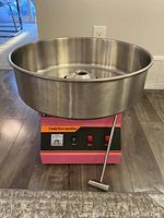 Full view of machine with stainless steel bowl and pink base on wood floor.