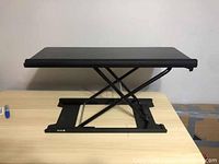 Side view of the black Vivo adjustable keyboard riser raised to a mid-level height showing the scissor-lift metal frame.