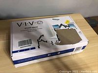 Box of VIVO STAND-V002K dual monitor desk mount showing product name and image on top of white and blue box with some damage.