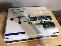 Closed original box of Vivo STAND-V003J triple monitor desk stand featuring an image of the assembled monitor stand clamping to a desk and holding three monitors.