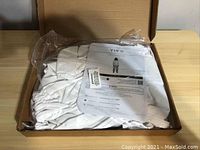 Packaged large full body beekeeping suit folded inside an open cardboard box with instruction paper on top.