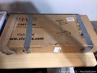 Photo of unopened brown cardboard box featuring printed illustrations and description of the Vivo CART-V04C mobile projector and laptop cart, secured with gray duct tape.