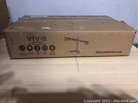 Sealed cardboard box with VIVO branding and product illustration showing dual monitor stand design.