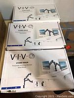 Photo shows two boxed VIVO pneumatic dual monitor desk mounts labeled Stand-V002K with product images illustrating dual monitor setup on desk mount arms.
