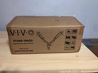 Box labeled VIVO Stand-V0020 Dual Monitor Desk Mount on wood table