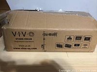 Sealed cardboard box of the VIVO stand model V001M showing product name, usage, and specifications on the side