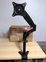 Front view of VIVO monitor desk mount stand attached to wooden desk with original packaging box behind.
