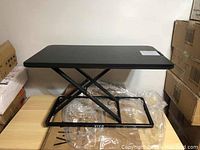 Full view of black adjustable desk riser with X-frame base on packaging.