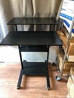 Full view of black VIVO stand up desk on caster wheels showing two main shelves and top additional shelf.