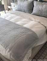 Bed with two icy blue-grey patterned pillow shams and a matching throw at foot of bed in light neutral room