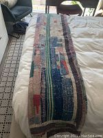 Kantha blanket fully spread out on bed showing patchwork and embroidery detail with a mix of green, blue, red, and cream colors in rectangular strips and blocks.