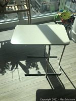 White rectangular side table with chrome metal frame in bright sunlight on light wood floor.