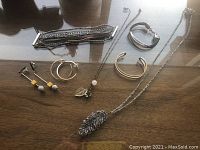 Overview of two necklaces with pendants, three bracelets, and two pairs of earrings laid on a wooden surface