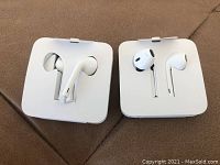 Two unopened pairs of Apple earbuds with mic in original white packaging holders.