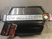 T-fal OptiGrill+ closed electric indoor grill with digital control panel showing cooking mode icons and doneness selection knob