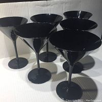 Photo showing six black glass martini glasses arranged in two rows.