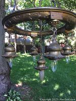 Full view of brass chandelier suspended outdoors against tree, showing circular frame, chains, and all five lights.