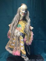 Full front view of the Chinese opera doll showing the detailed yellow embroidered costume with pink feather trim and the figure's long hair.