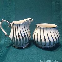 Silver swirl pattern creamer and sugar set on fabric background showing side view.