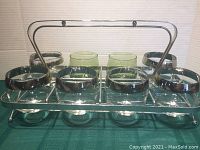 Front view of chrome caddy holding 8 glasses, 6 clear with silver bands, 2 green swirl